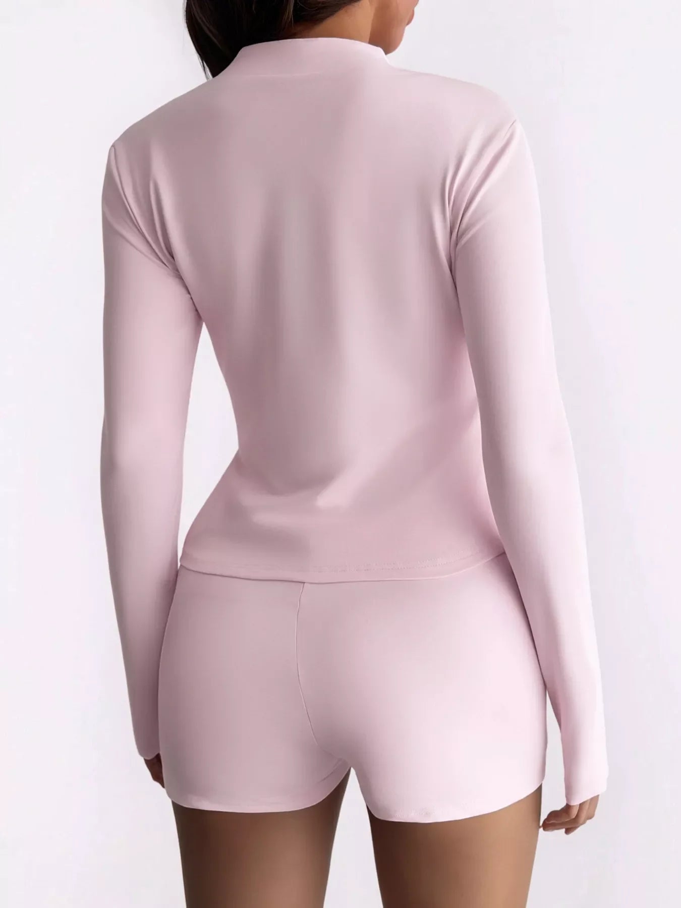 Back view of woman wearing light pink long-sleeve top and matching shorts on white background