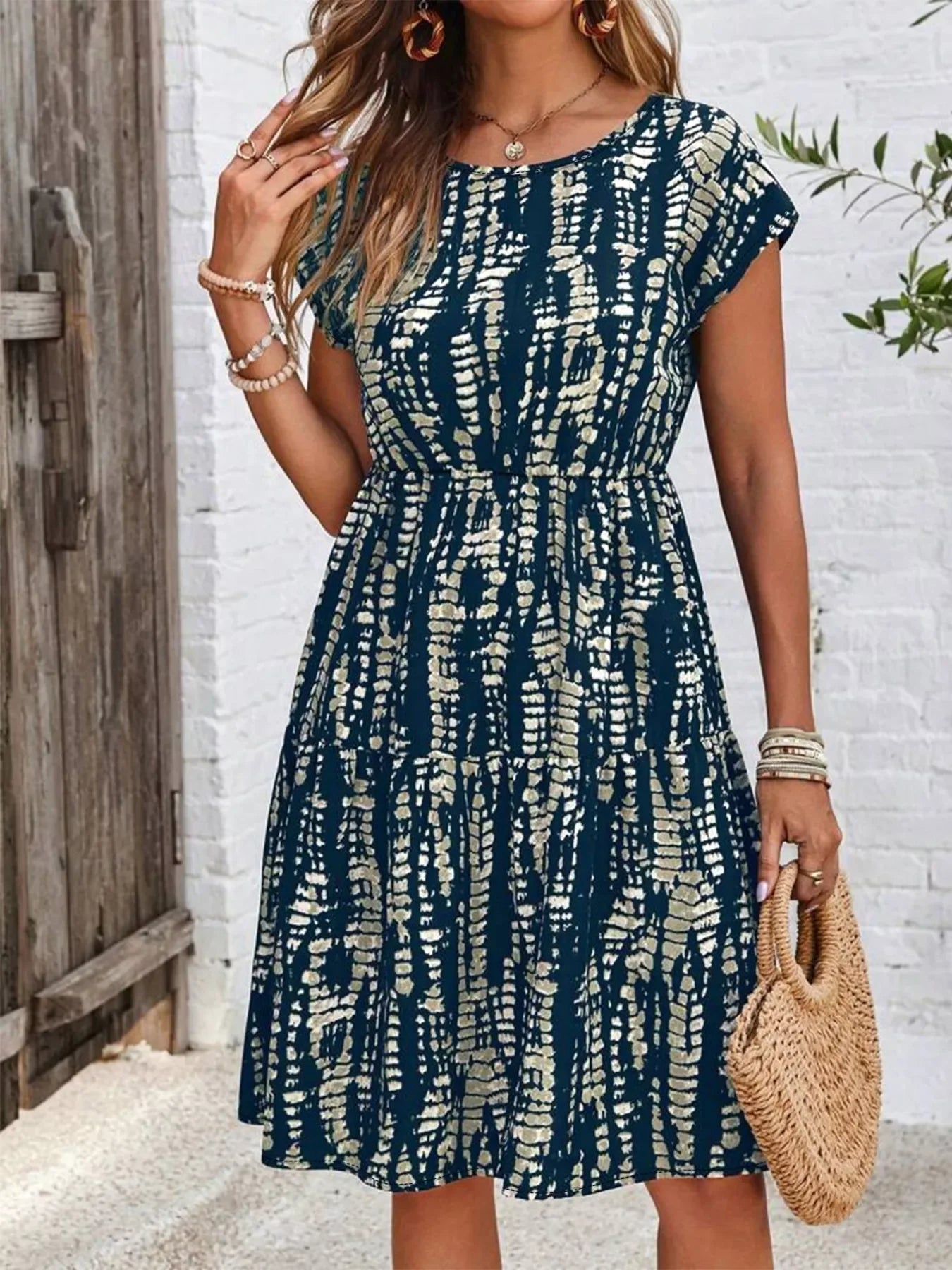 Woman wearing a navy blue and beige patterned casual dress holding a round woven handbag