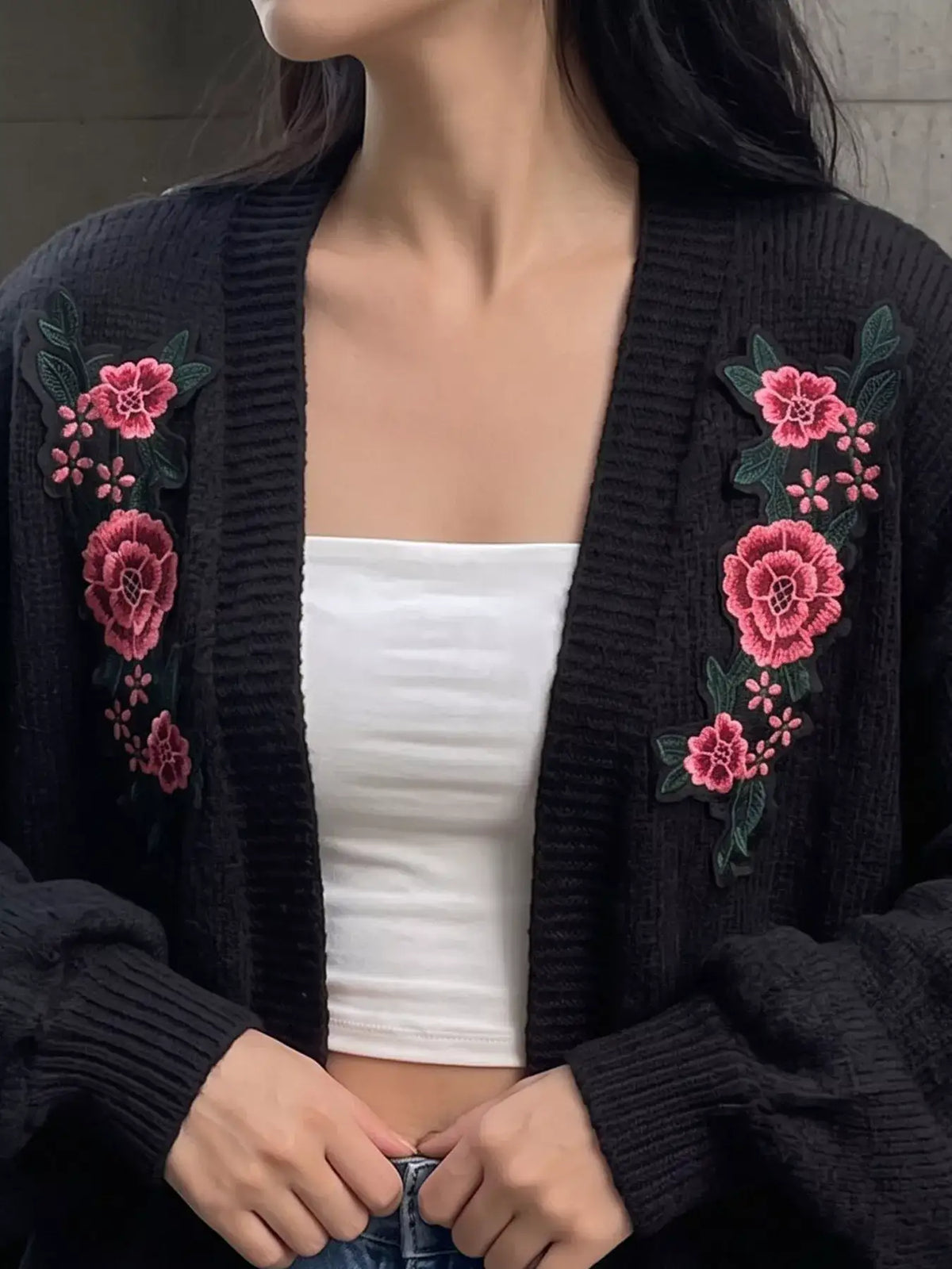 Black knit cardigan by Evie's Dreamland with pink floral embroidery, worn over a white tube top.
