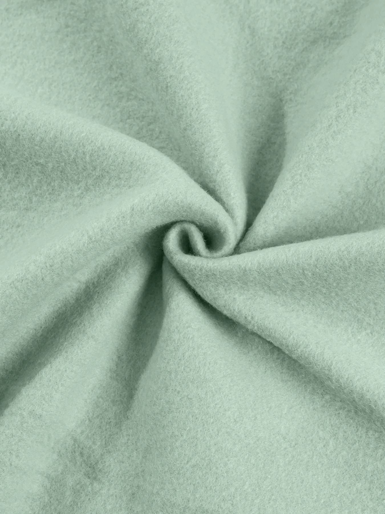 Close-up of soft light green wool fabric twisted in the center showing texture and fibers