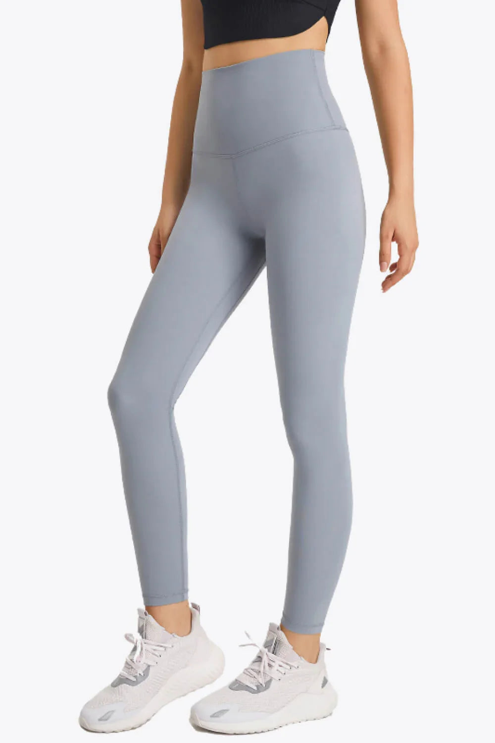 Woman wearing high-waisted gray leggings and white athletic sneakers against white background