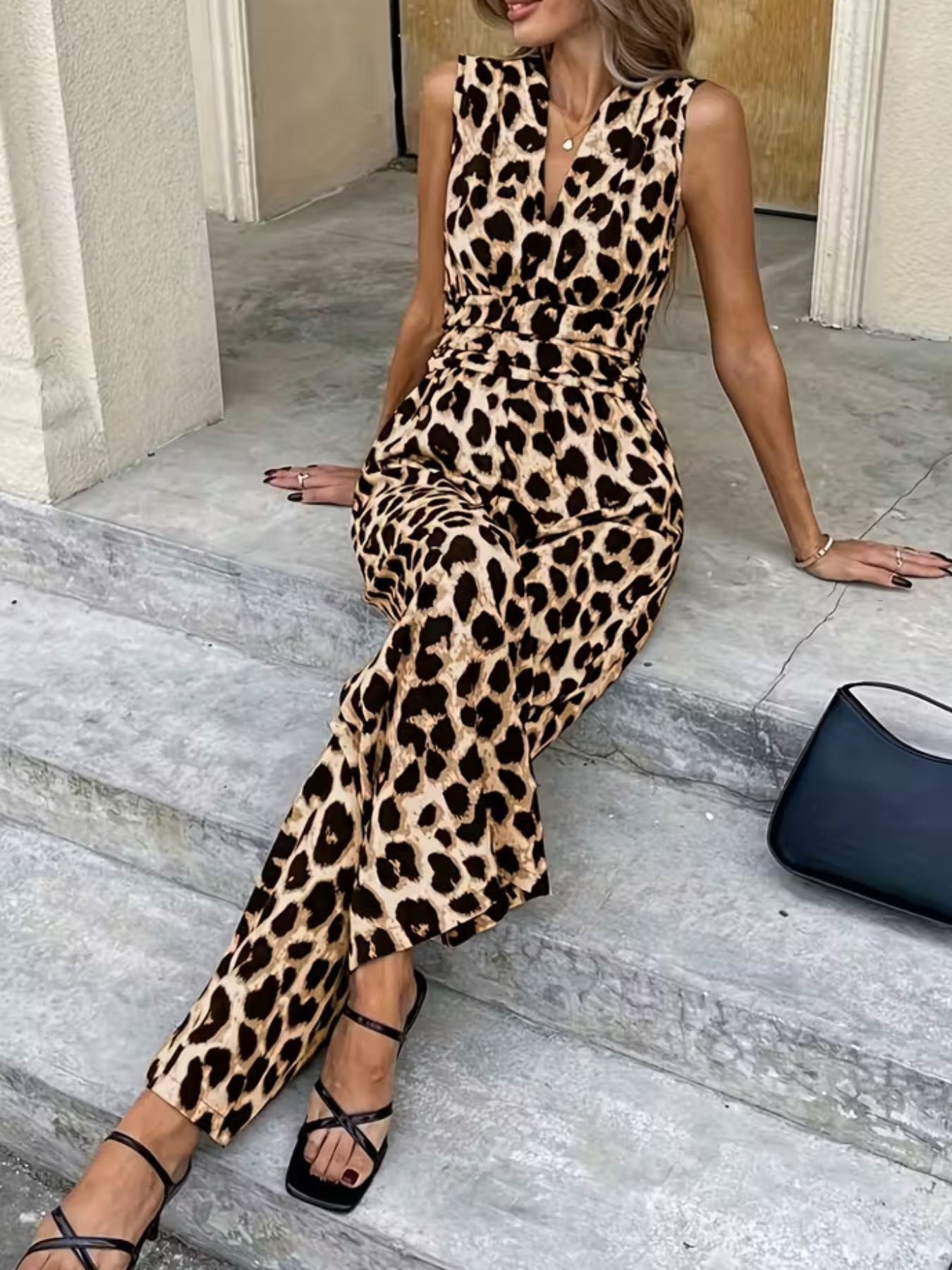 Woman wearing sleeveless leopard print jumpsuit and strappy sandals sitting on steps