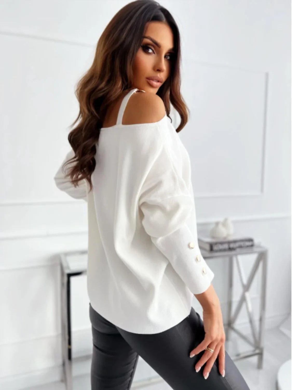 Woman wearing off-shoulder white sweater with gold button details and black faux leather pants