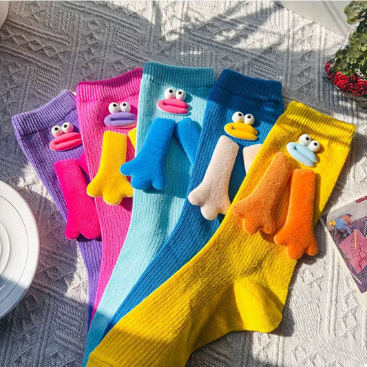 Colorful knitted socks with cartoon duck faces and webbed feet designs, laid on a patterned surface