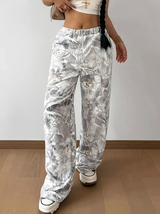 Woman wearing loose abstract print wide-leg pants with chunky white sneakers on wooden floor