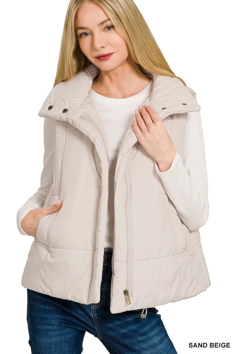 Woman wearing sand beige quilted puffer vest with zipper and snap buttons, paired with white long sleeve shirt and blue jeans