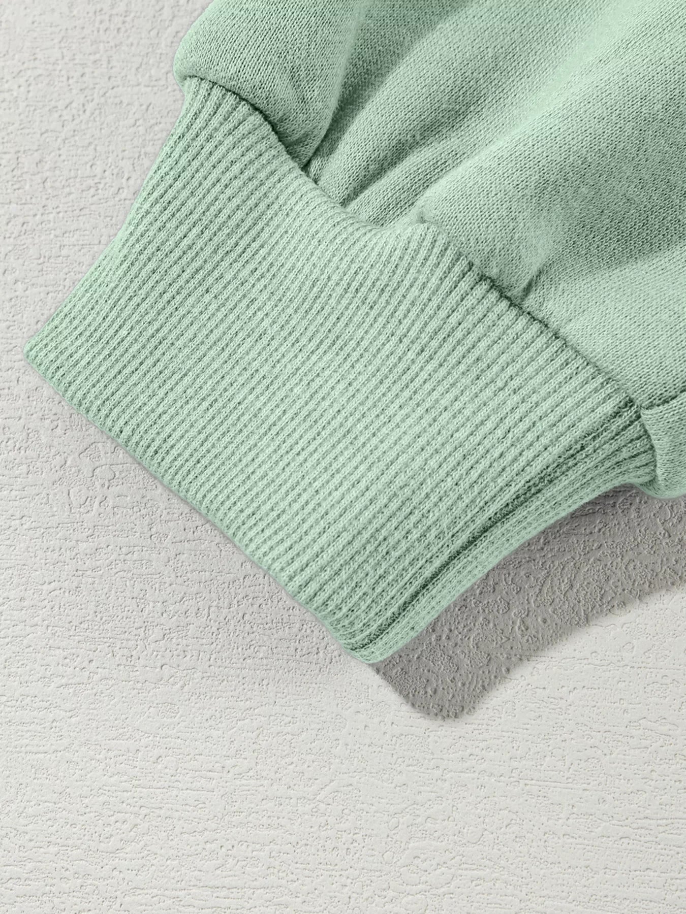 Close-up of a mint green ribbed cuff on a soft fabric sleeve on textured white surface
