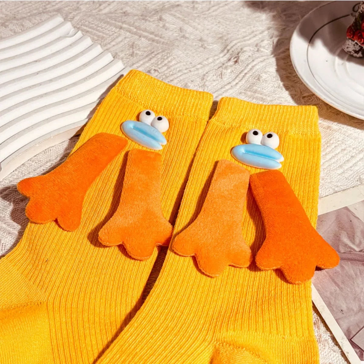 Bright yellow socks with 3D orange duck feet and blue beak designs on ribbed fabric