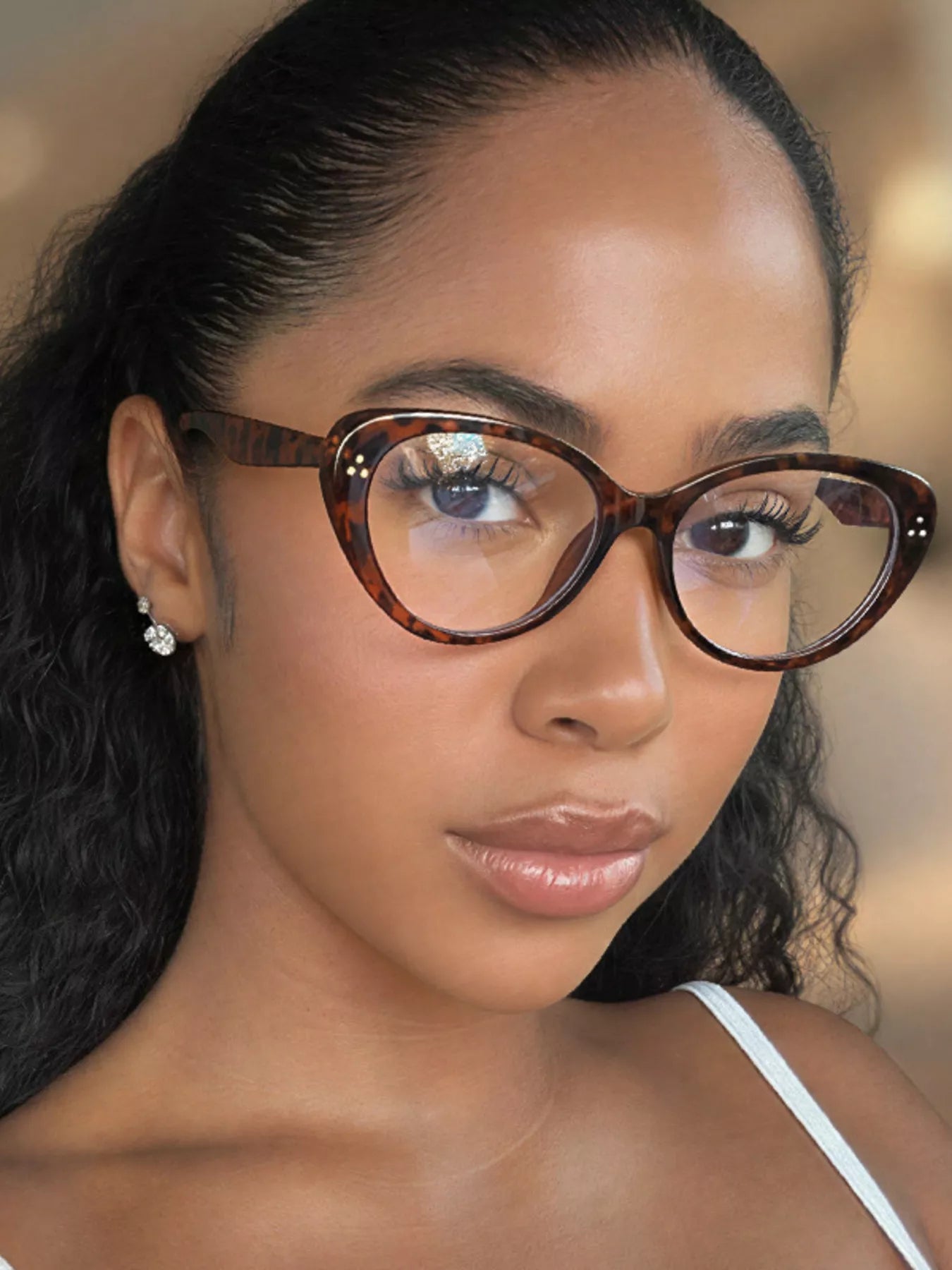 Woman wearing tortoiseshell cat-eye glasses and small crystal earrings.