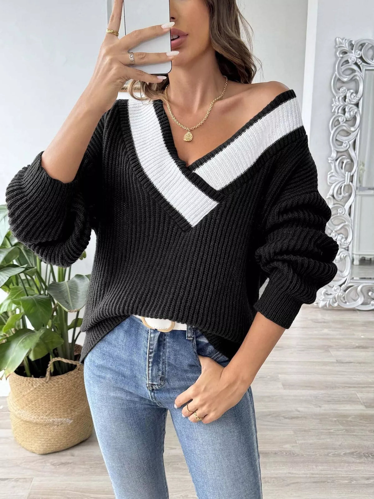 Women's black ribbed V-neck sweater with white contrast trim and balloon sleeves, styled with blue jeans.
