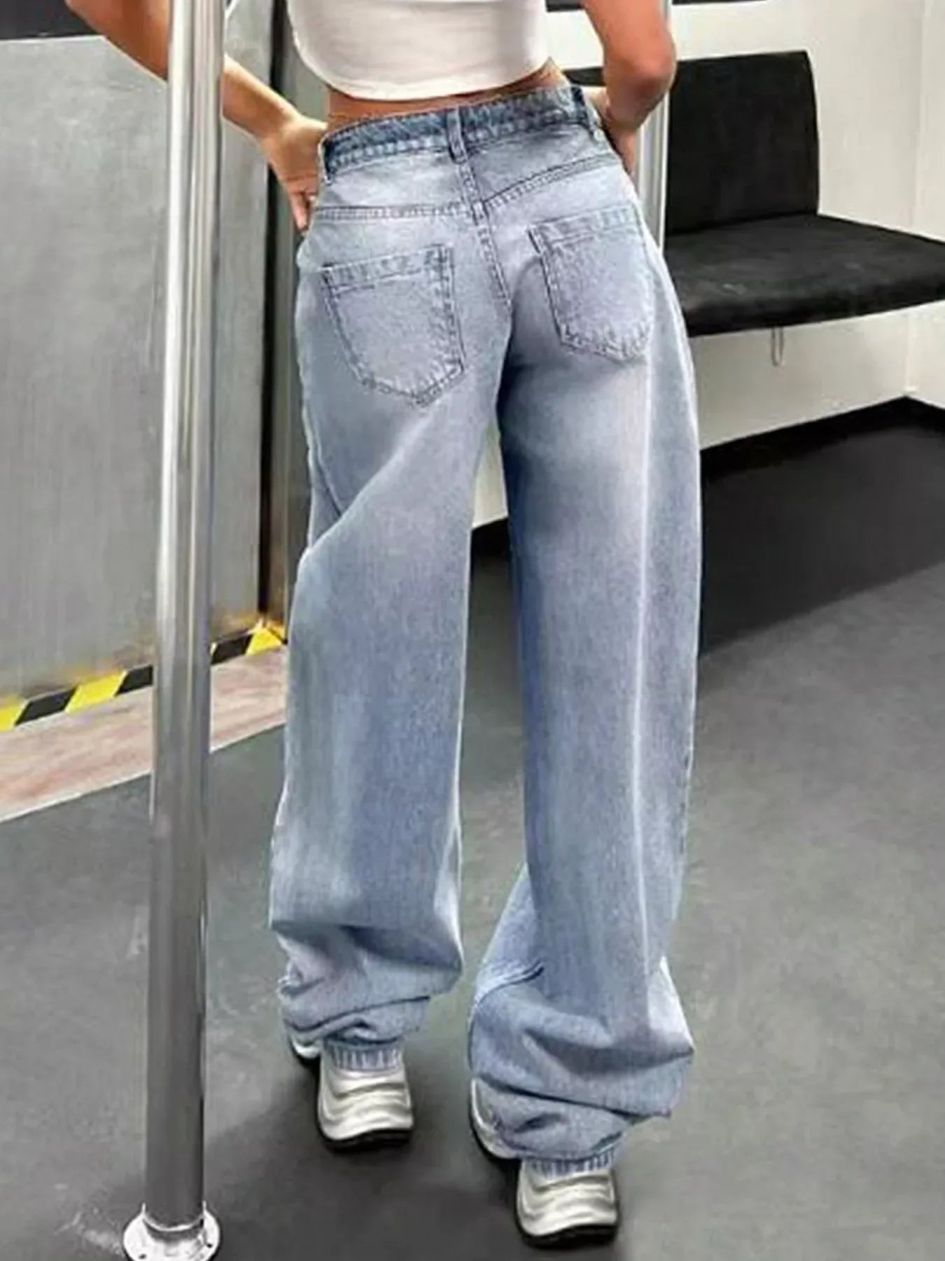 Woman wearing light blue baggy jeans and white sneakers in urban indoor setting