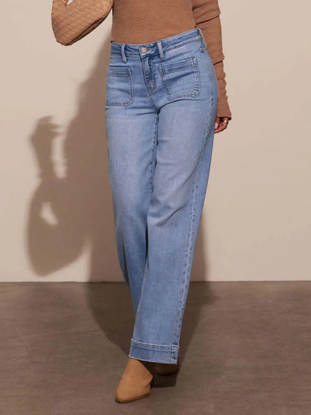 Woman wearing wide-leg light blue jeans with front patch pockets and tan ankle boots