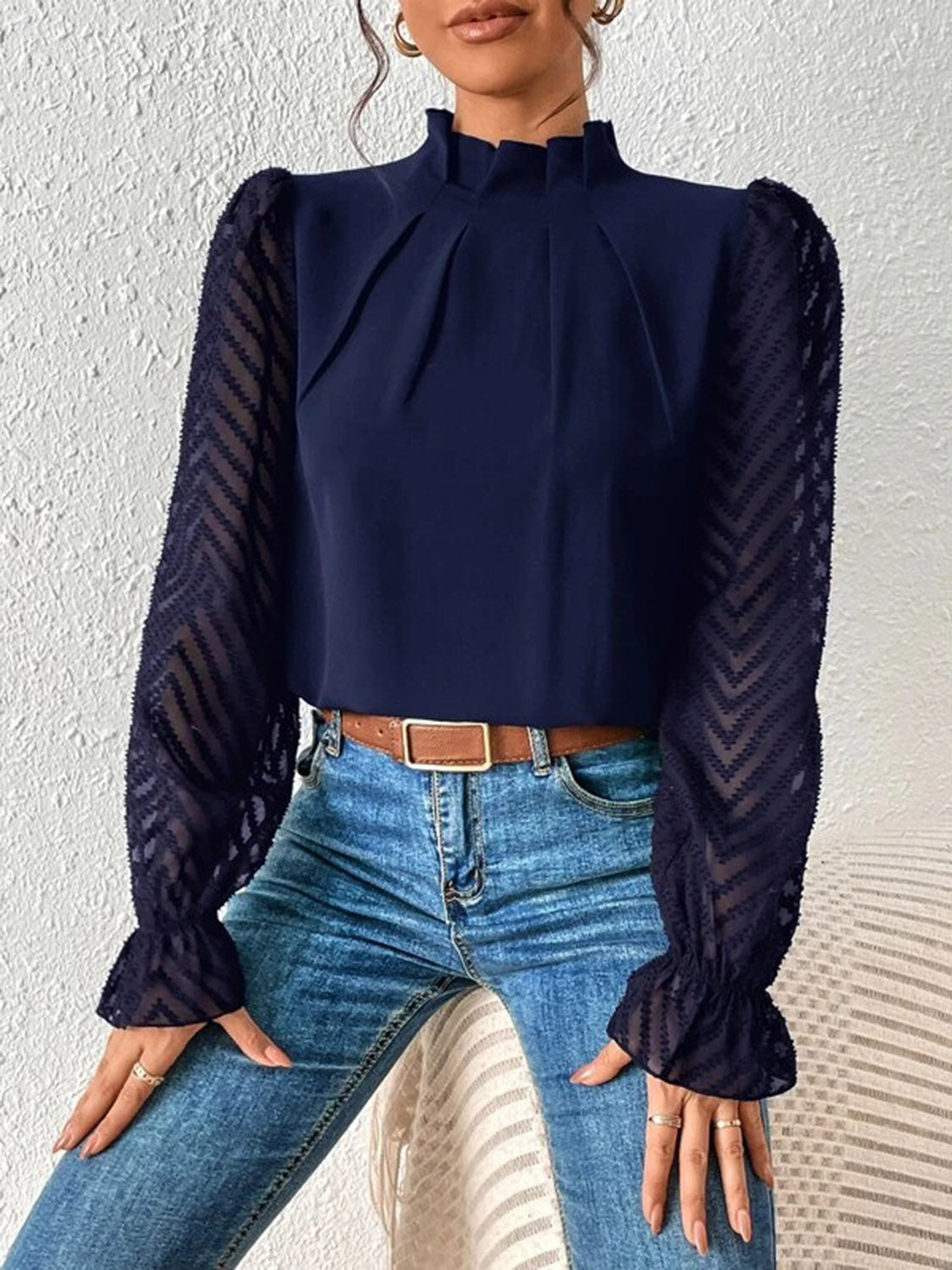Woman wearing a navy chiffon blouse with sheer chevron sleeves and blue jeans