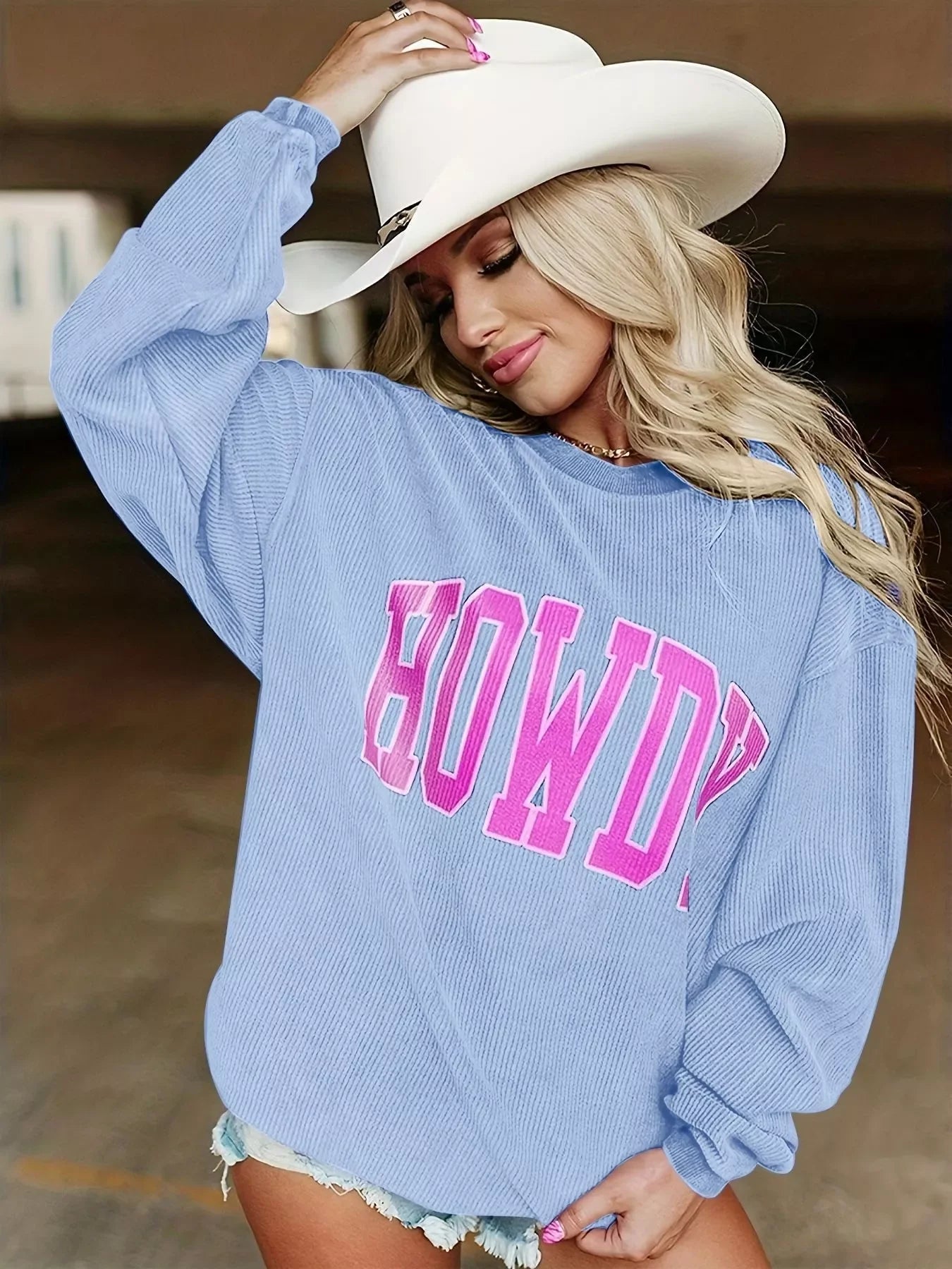 Blonde woman wearing a white cowboy hat and blue sweatshirt with pink HOWDY lettering