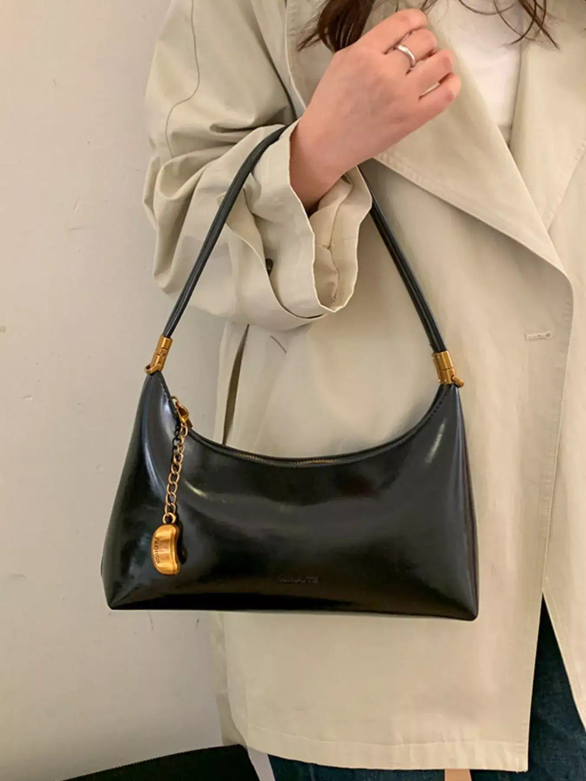 Black PU leather shoulder bag with gold chain charm, styled with a beige trench coat.