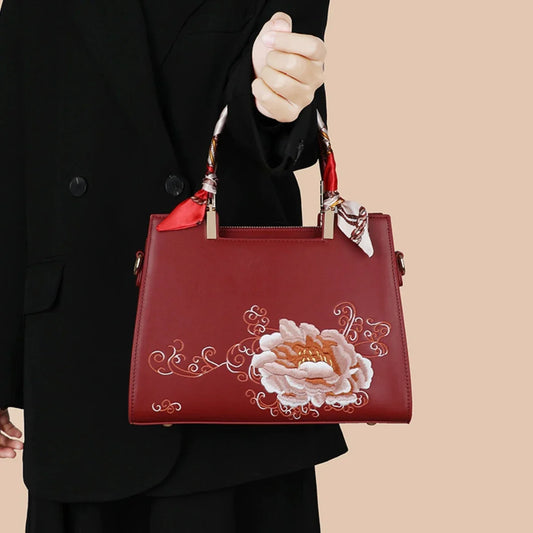 Red embroidered floral handbag with scarf-wrapped handles held by woman in black coat