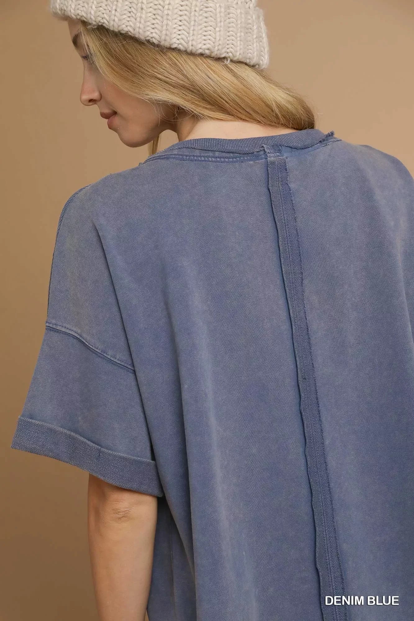 Close-up of woman wearing denim blue oversized t-shirt and cream knit beanie against beige background