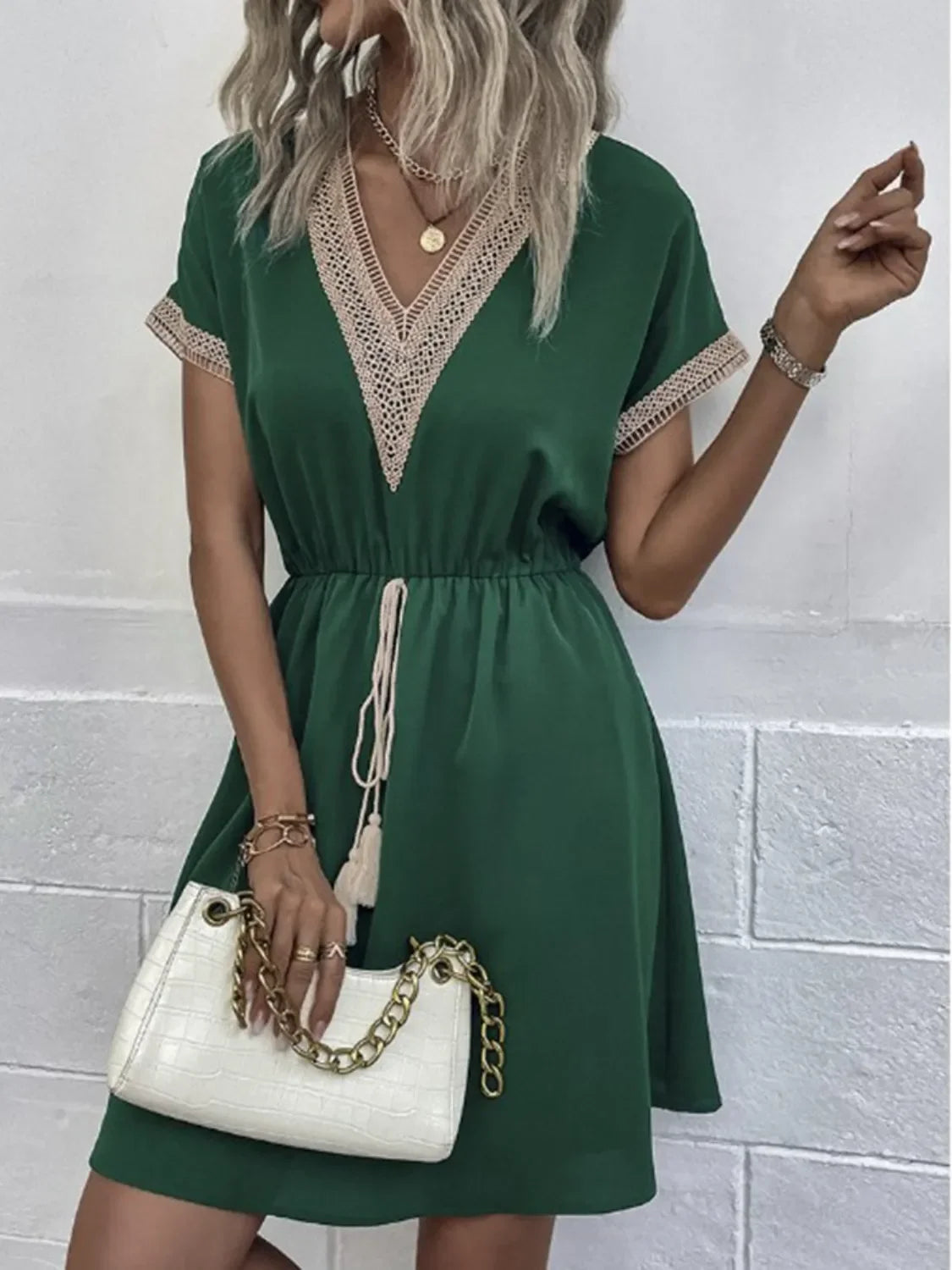 Green V-neck dress with lace trim, paired with white chain-handle bag for chic everyday elegance.