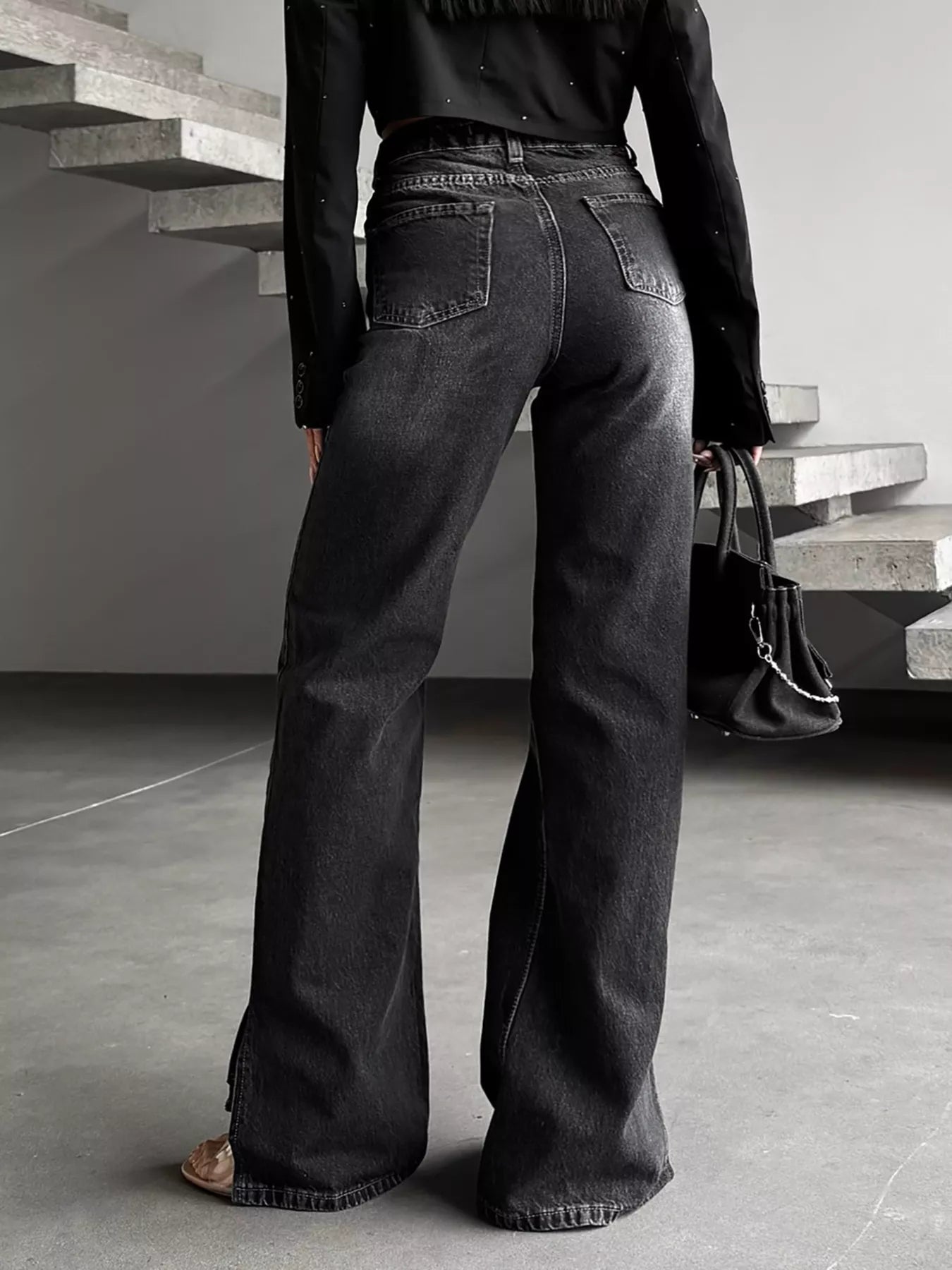 Woman wearing high-waisted black wide-leg jeans and holding a black handbag indoors.