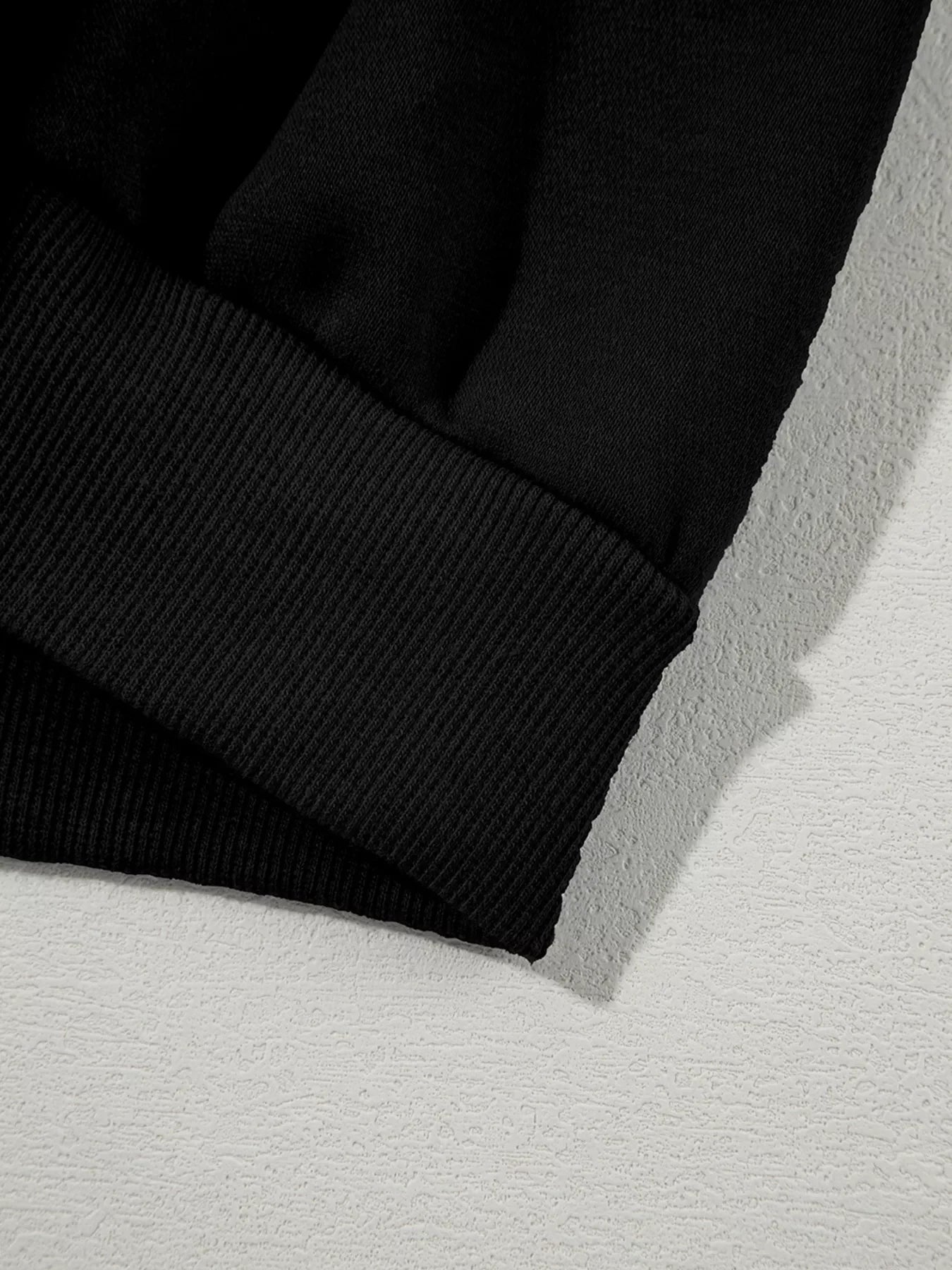 Close-up of black sweatshirt sleeve with ribbed cuff on textured white surface