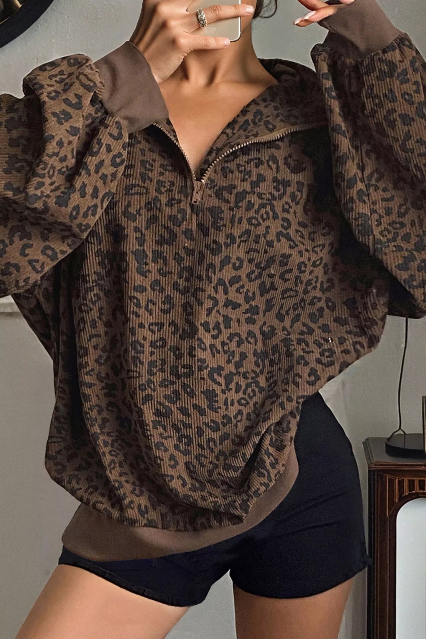 Woman wearing brown leopard print quarter-zip sweatshirt with ribbed texture and black shorts