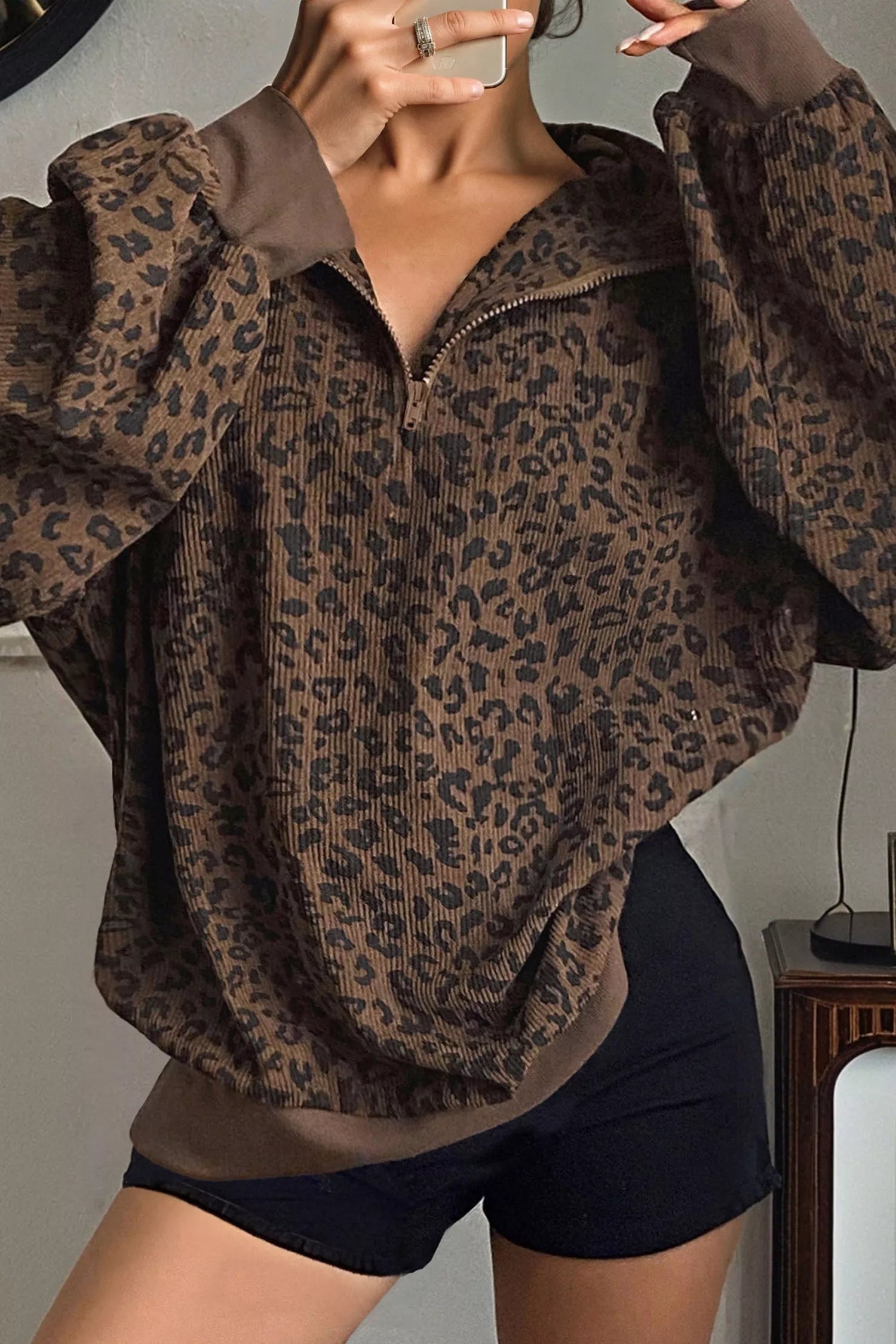 Woman wearing brown leopard print quarter-zip sweatshirt with ribbed texture and black shorts
