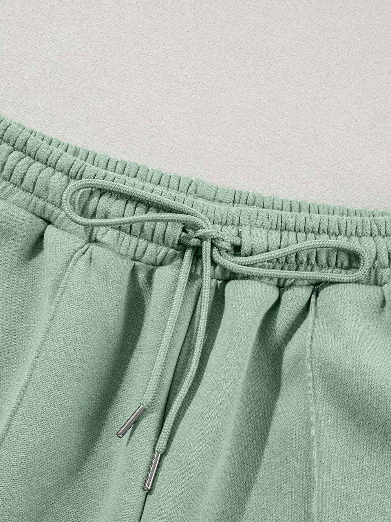 Close-up of sage green sweatpants waistband with elastic and tied drawstring
