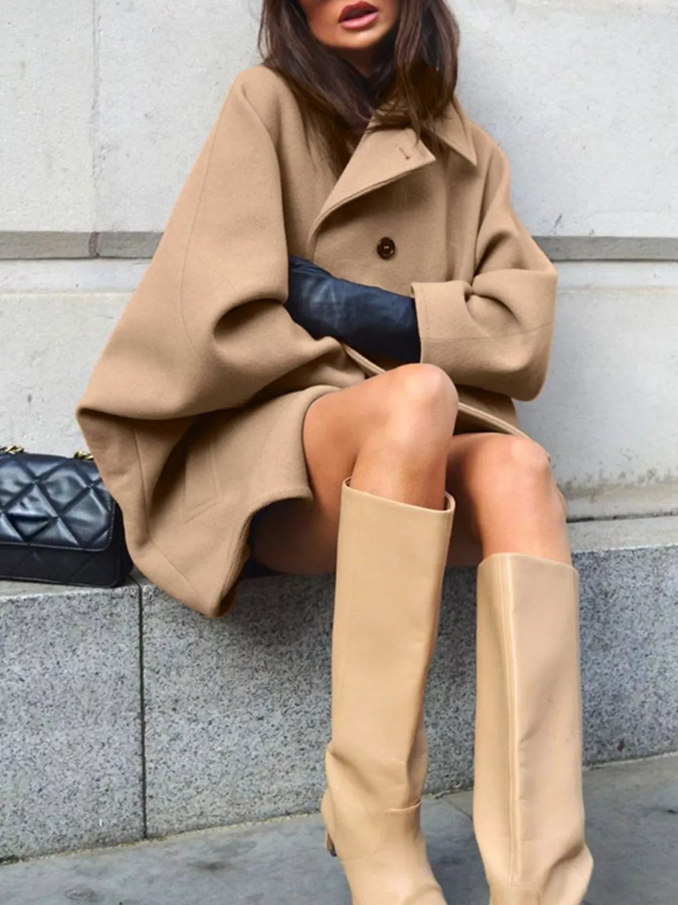 Woman wearing an oversized tan coat and matching knee-high boots with a black handbag
