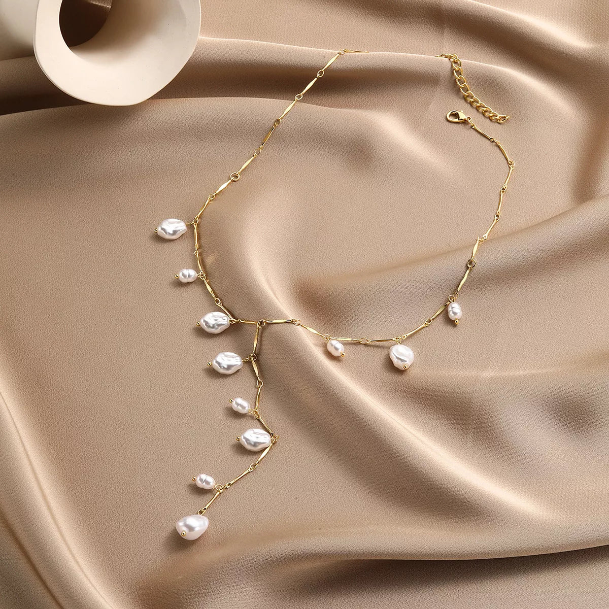 Elegant gold chain necklace with baroque pearls, styled on soft beige fabric for everyday chic fashion.