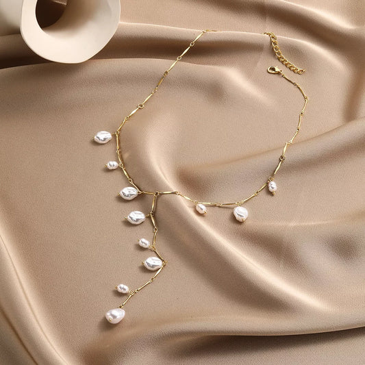 Elegant gold chain necklace with baroque pearls, styled on soft beige fabric for everyday chic fashion.