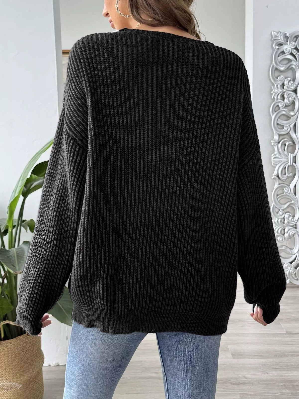 Back view of a woman wearing a black ribbed knit sweater from Evie's Dreamland and light blue jeans.