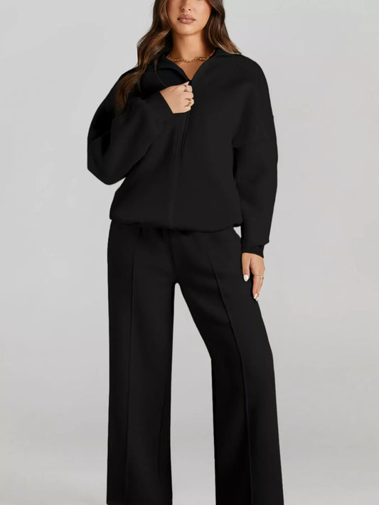 Woman wearing black zip-up jacket and wide-leg pants outfit with gold chain necklace