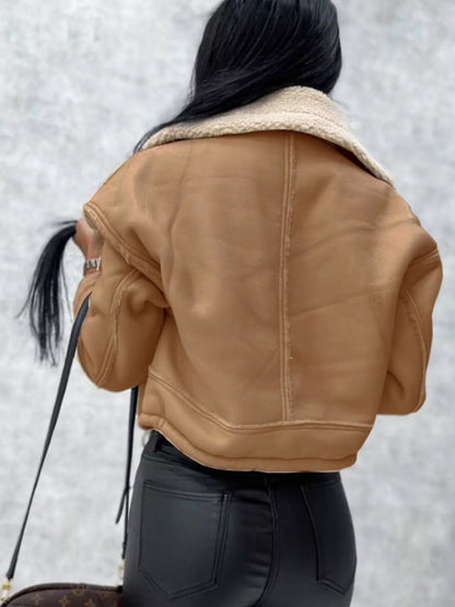 Woman wearing a cropped tan shearling jacket with black leather pants holding a designer handbag