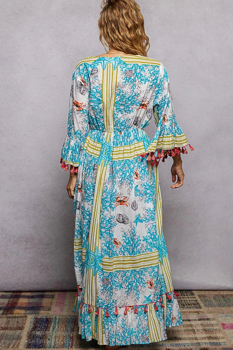 Woman wearing a long boho maxi dress with blue coral and seashell print, striped accents, and ruffled sleeves.