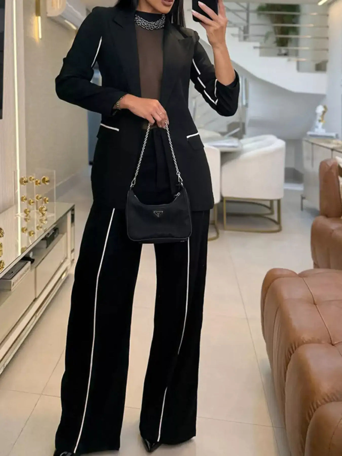 Evie's Dreamland black blazer and wide leg pants set with white contrast trim and a black handbag.