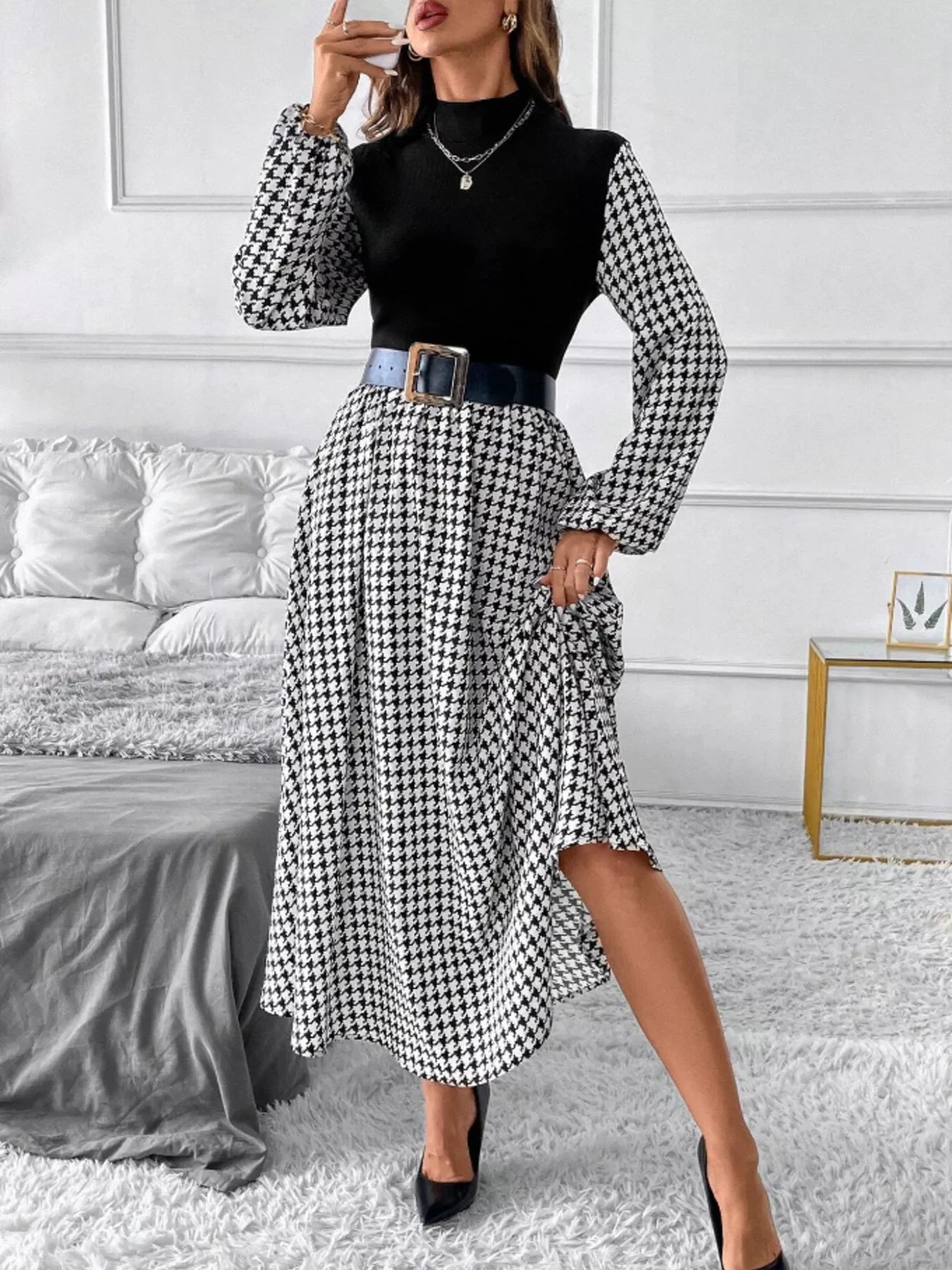 Woman wearing black top with houndstooth puff sleeves and skirt, black belt, and black heels in modern bedroom