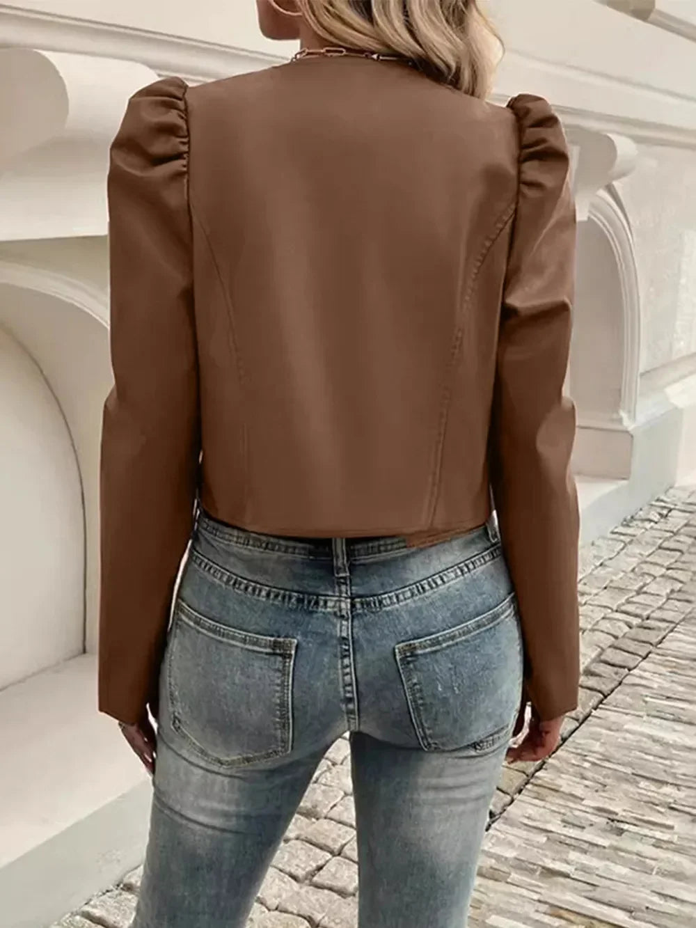 Back view of a woman wearing a brown cropped puff sleeve jacket and blue jeans.