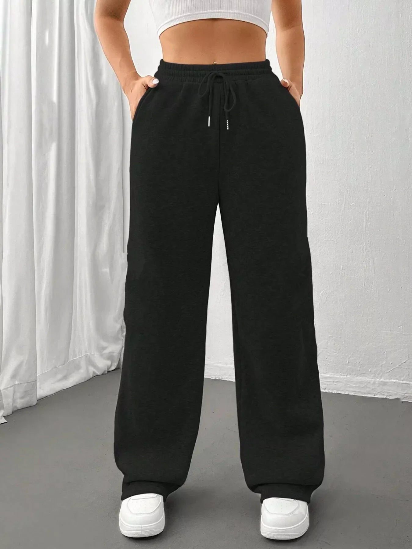 Woman wearing black wide-leg sweatpants with drawstring and white sneakers, standing indoors