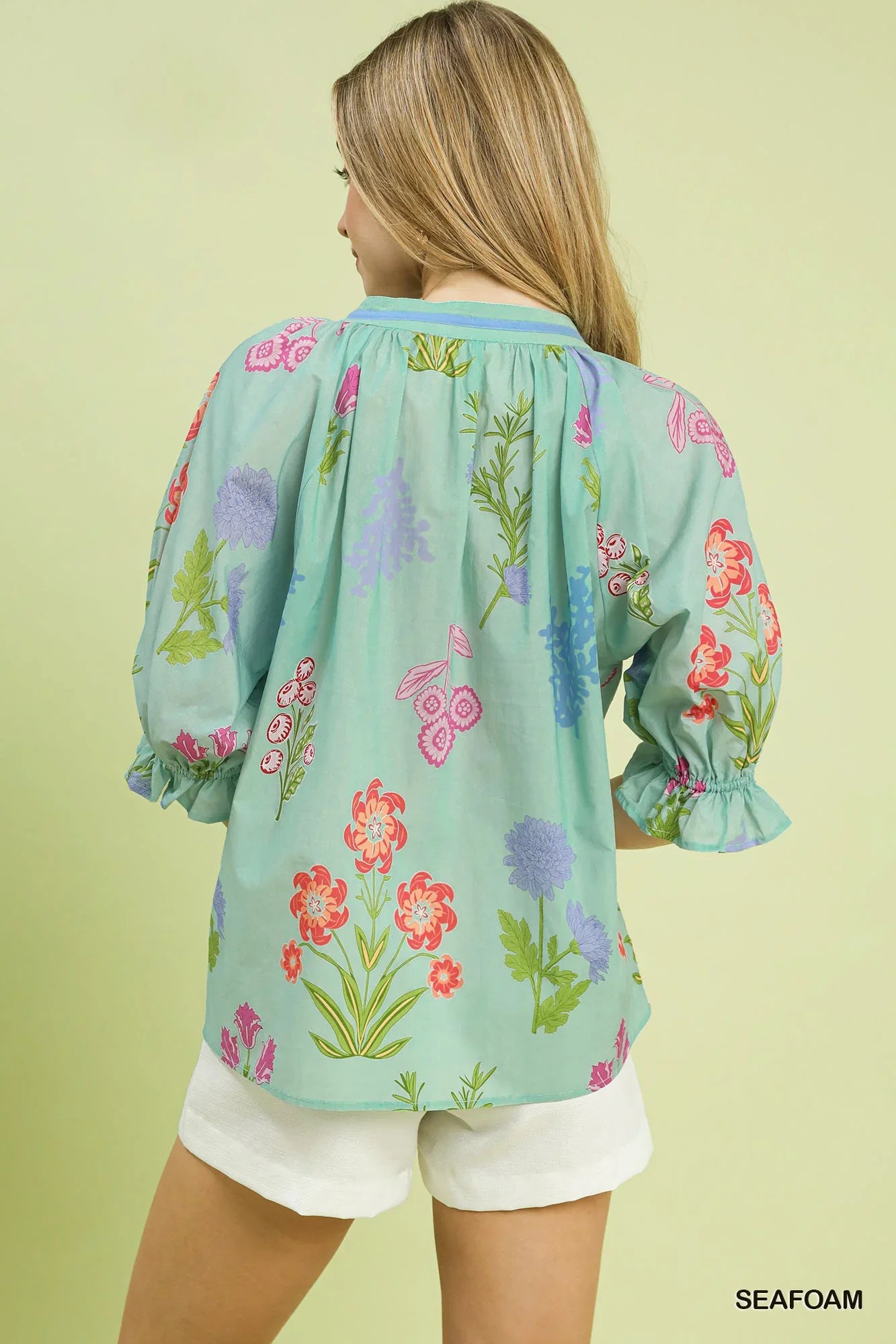 Woman wearing a seafoam green floral blouse with puff sleeves and white shorts