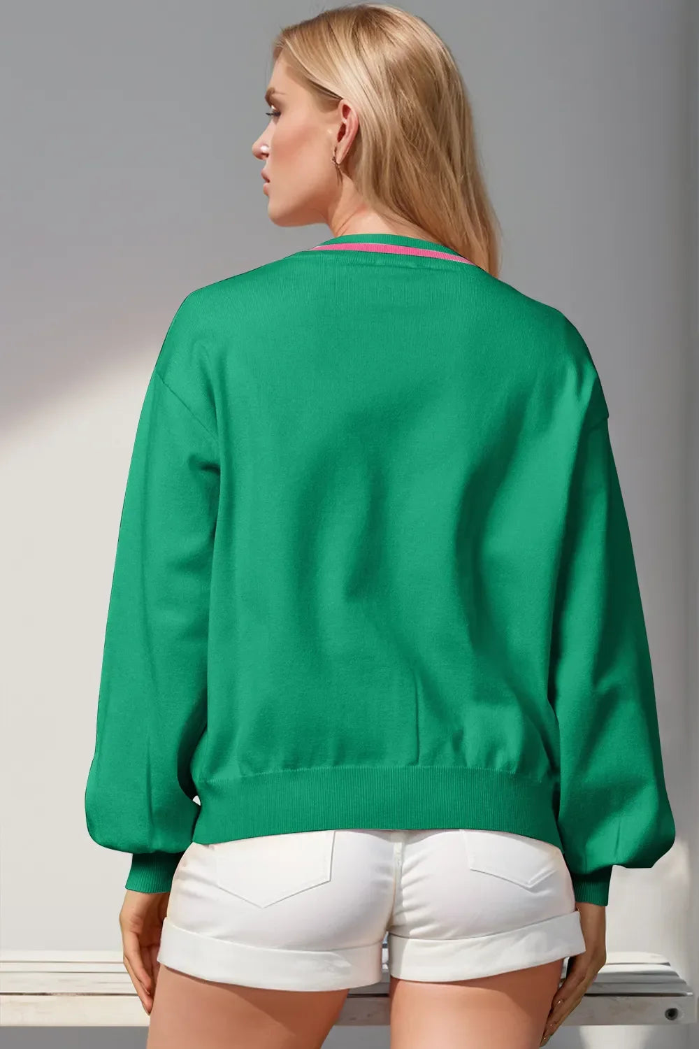Rear view of woman wearing green long-sleeve sweater and white rolled shorts in bright setting