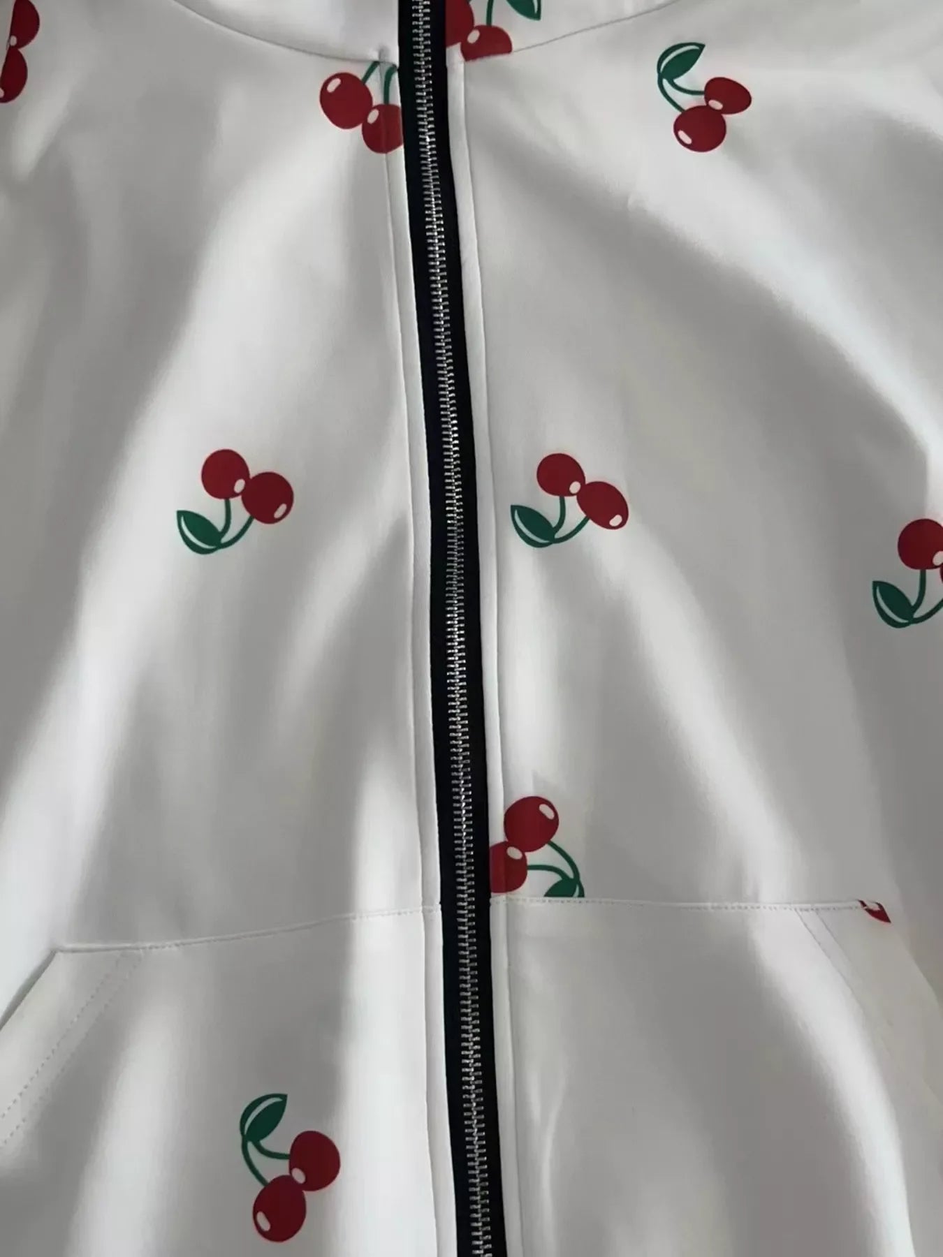 White zip-up hoodie with red cherry prints and green leaves, close-up detail of front zipper