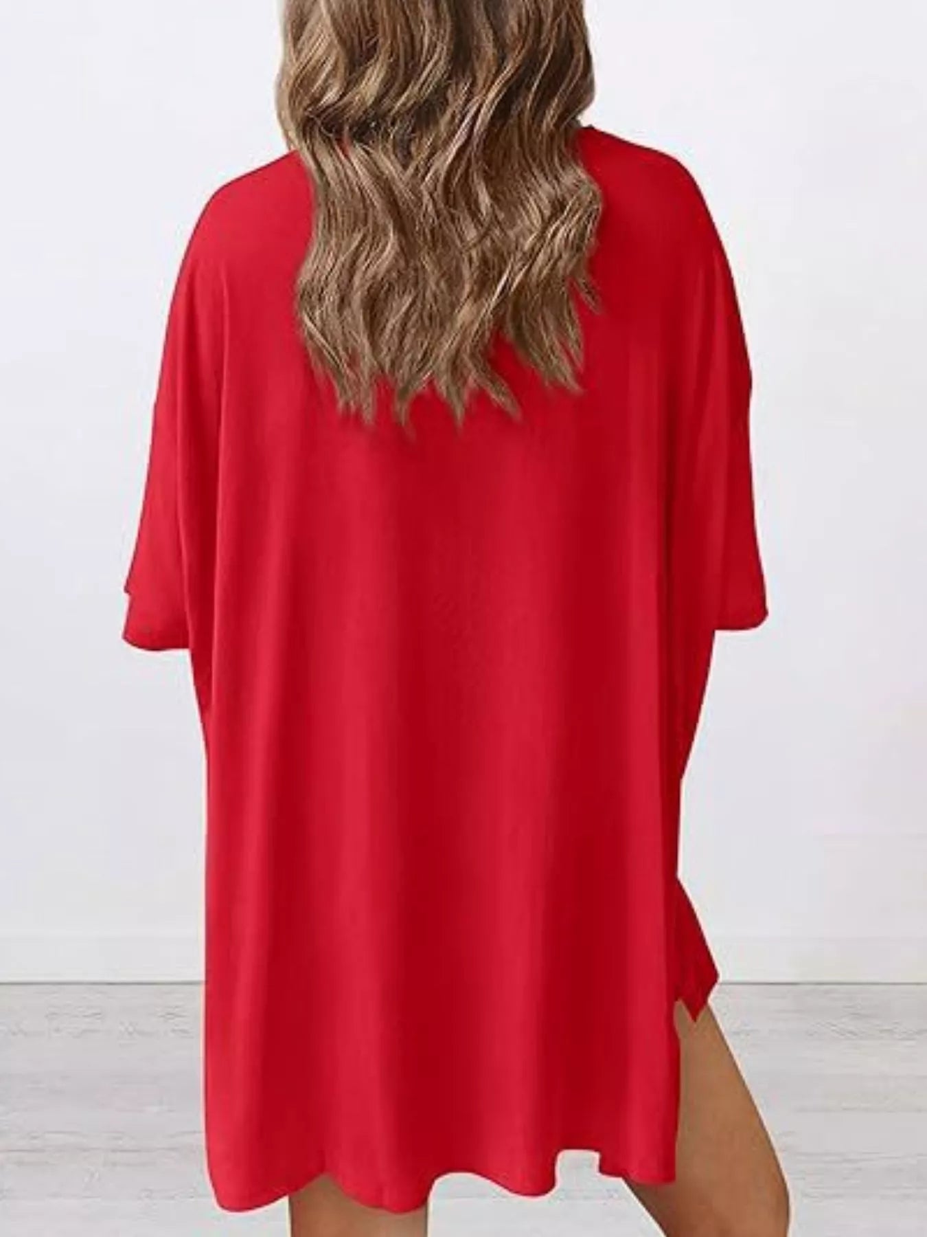 Woman wearing loose red oversized t-shirt dress, back view, in bright minimal room