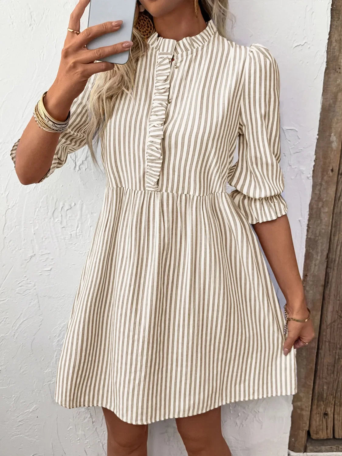 Woman wearing beige and white vertical striped dress with ruffled front and 3/4 sleeves