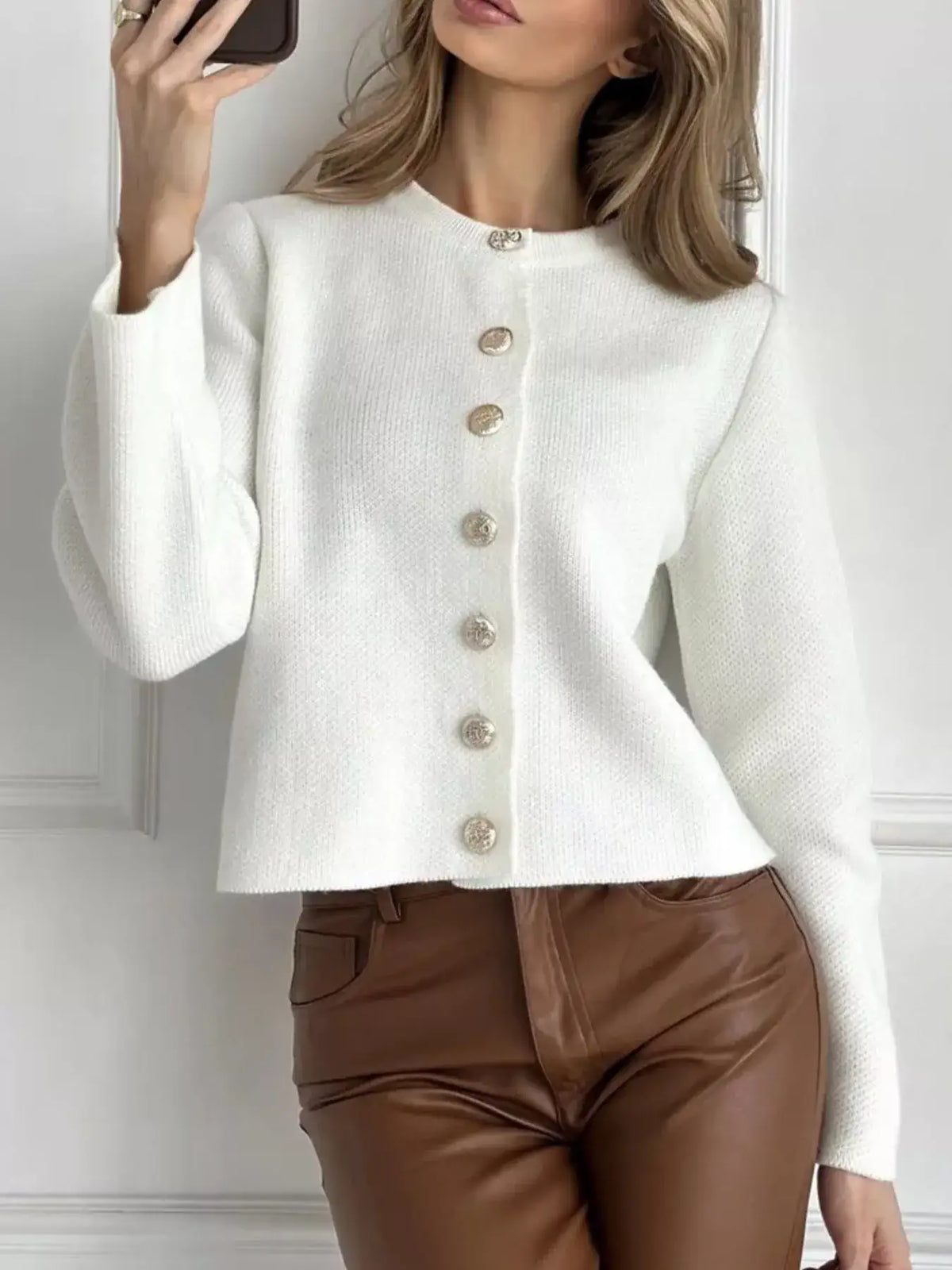 Woman wearing a white crew neck button down cardigan by Evie's Dreamland paired with brown leather pants.
