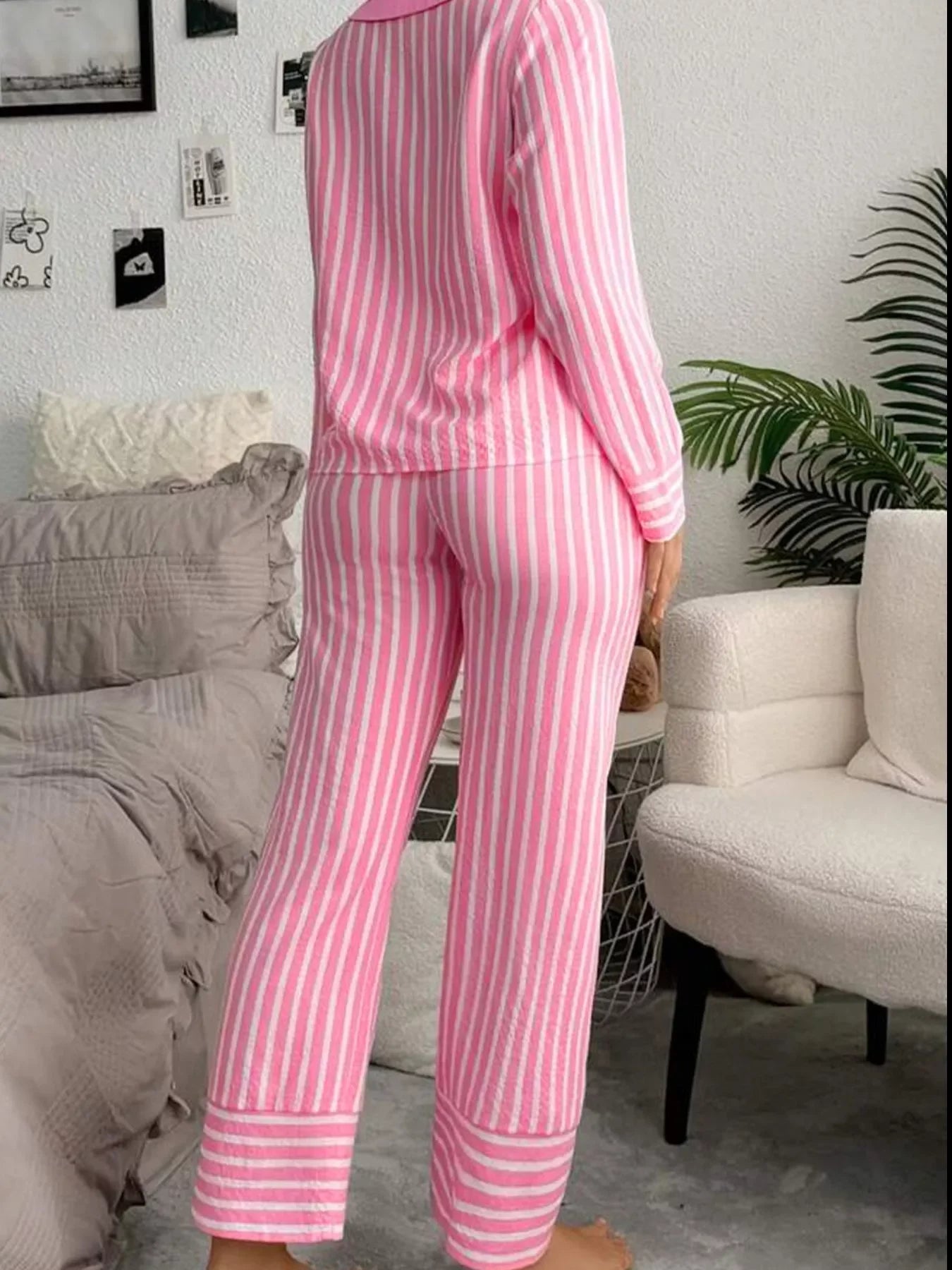 Person wearing pink and white striped pajama set standing indoors near beige bed and white armchair