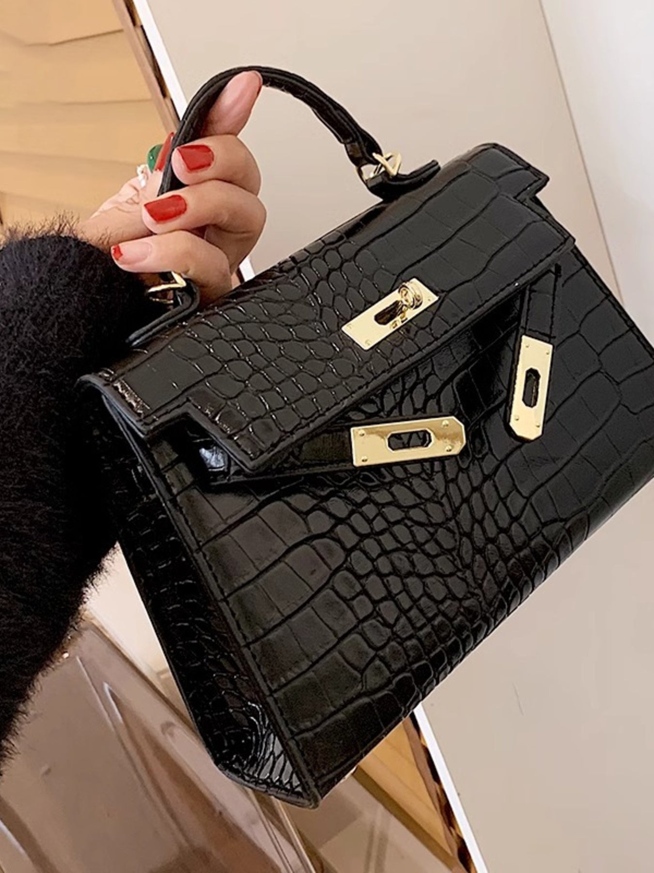 Woman holding a black crocodile pattern handbag with gold hardware and top handle