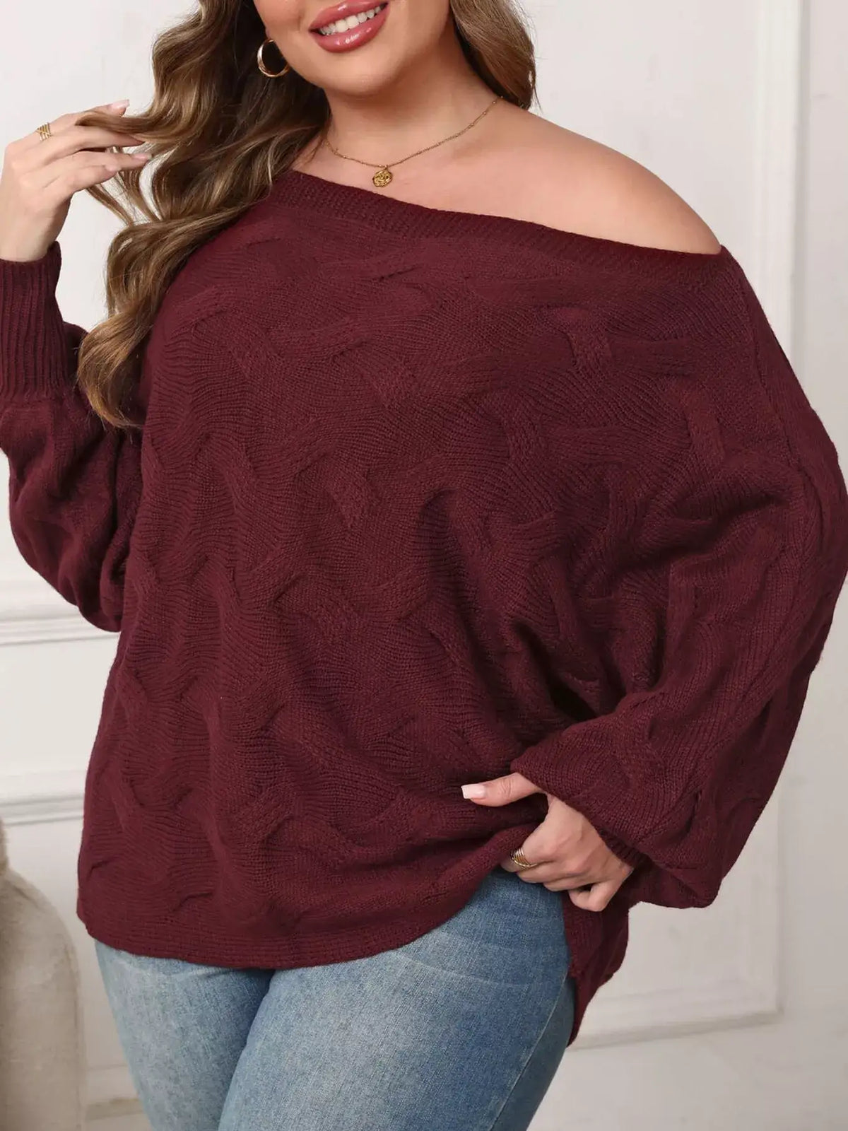 Plus size burgundy off-shoulder long sleeve cable knit sweater by Evie's Dreamland paired with blue jeans.