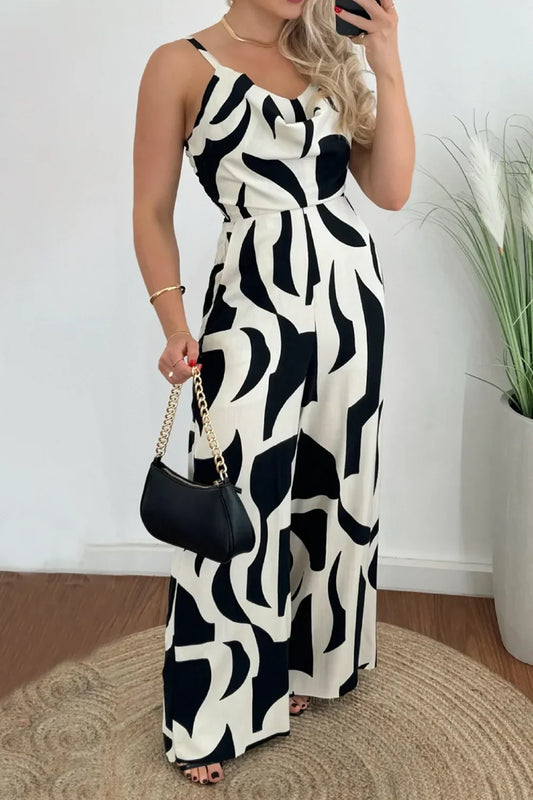Woman wearing black and white abstract print jumpsuit holding black handbag with gold chain indoors