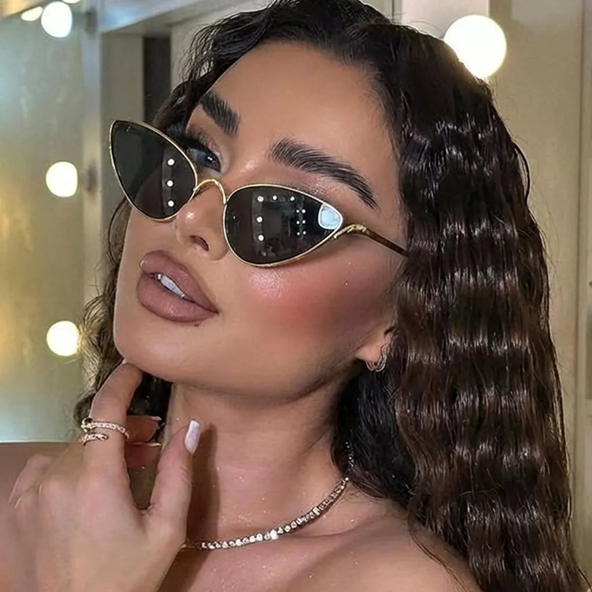 Woman wearing gold-rimmed black cat eye sunglasses and a sparkling necklace.