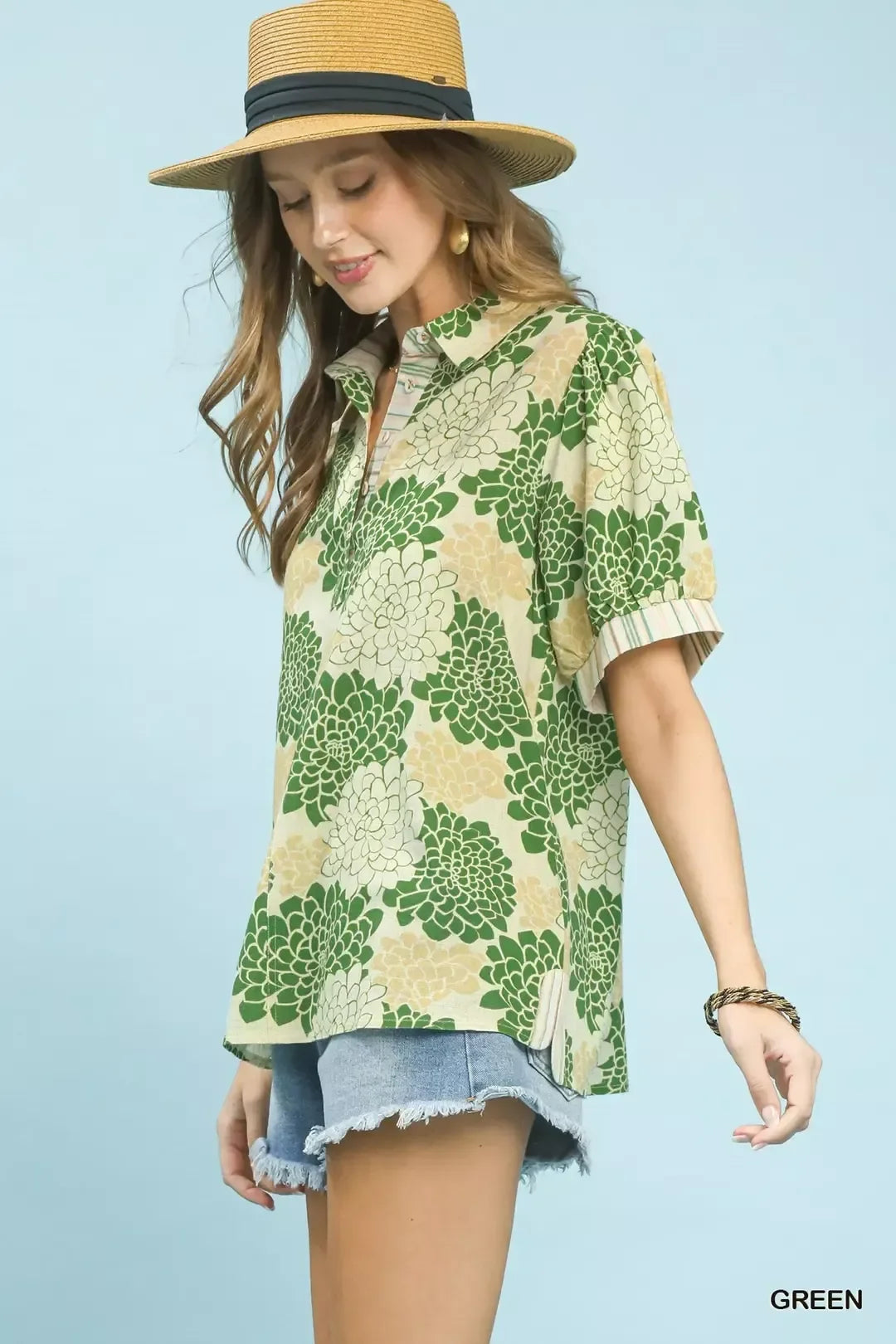 Woman in straw hat wearing green floral print blouse and denim shorts, casual summer outfit